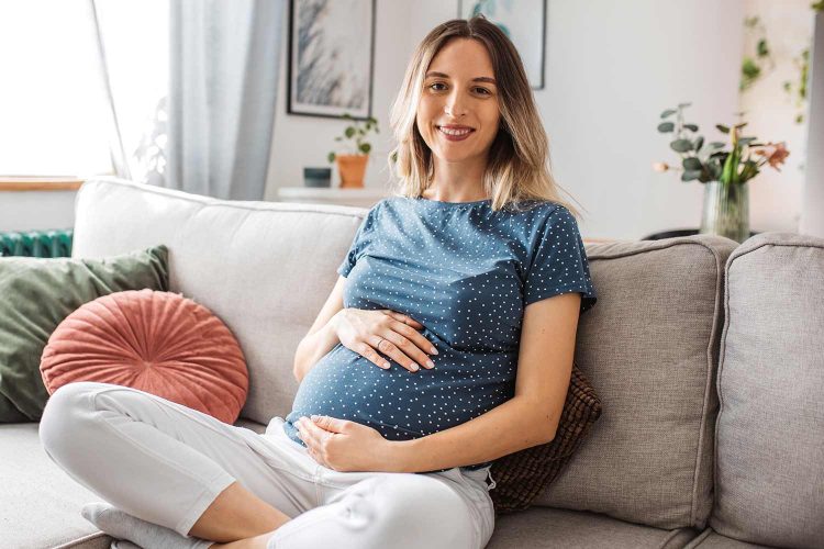 schwanger Frau auf Sofa mit Händen auf dem Bauch